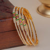 Four gold-plated bangles adorned with clear rhinestones and green and pink floral accents, displayed on a dark wooden box.